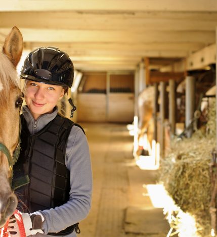 Young female rider with horse inside stable