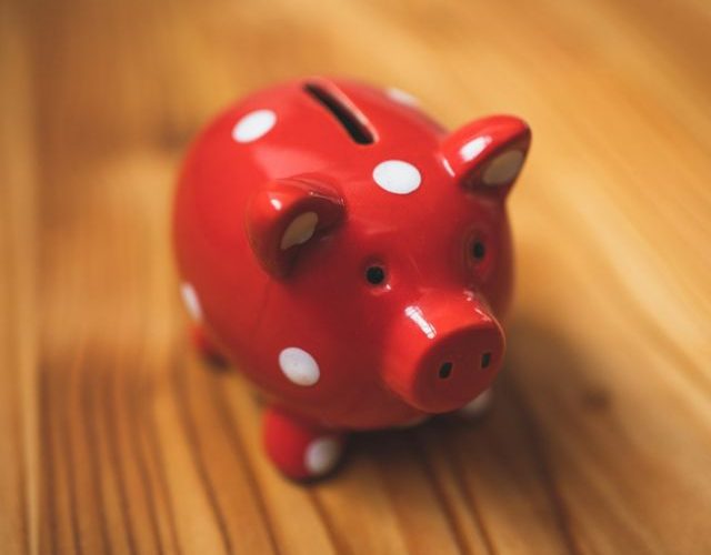 Image of a red ceramic piggy bank on a wooden desk.